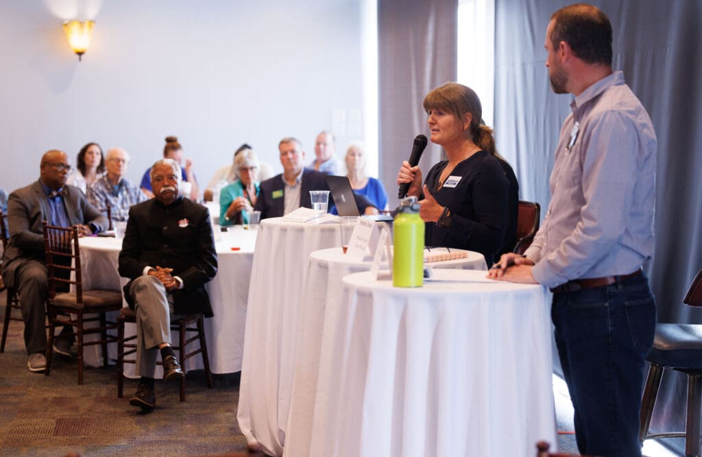 Hannah Ordos speaks with a microphone in hand at a table with a white tablecloth.