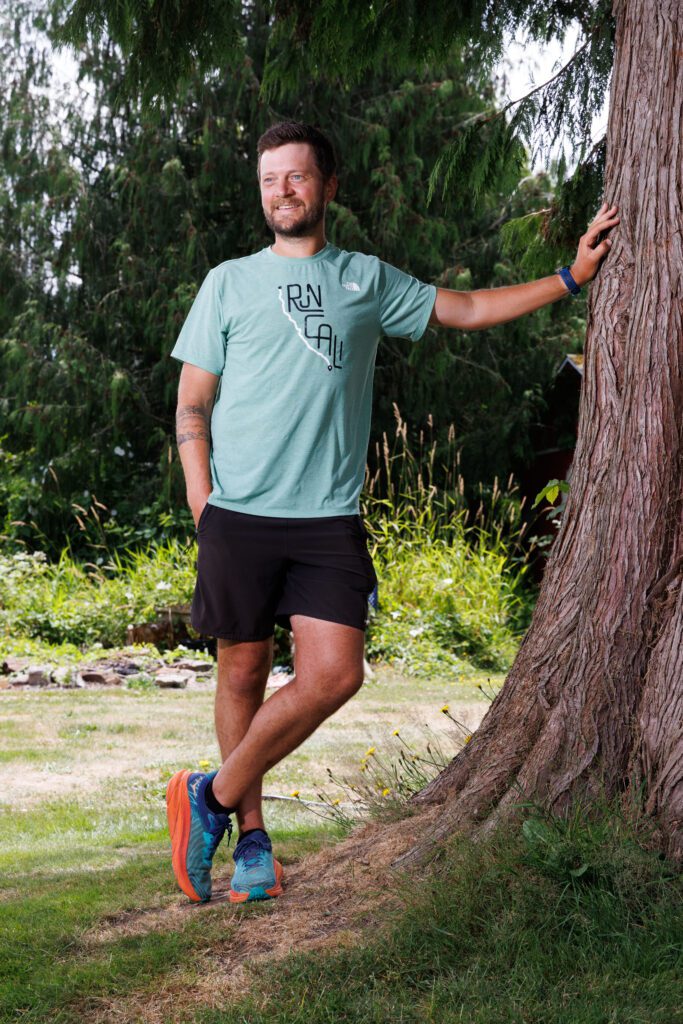 Marcus Nuckolls leans against a tree while wearing a "Run Cali" shirt.