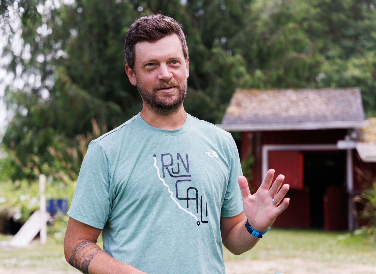 Marcus Nuckolls talks as he gestures with his hands in front of a small red shed.