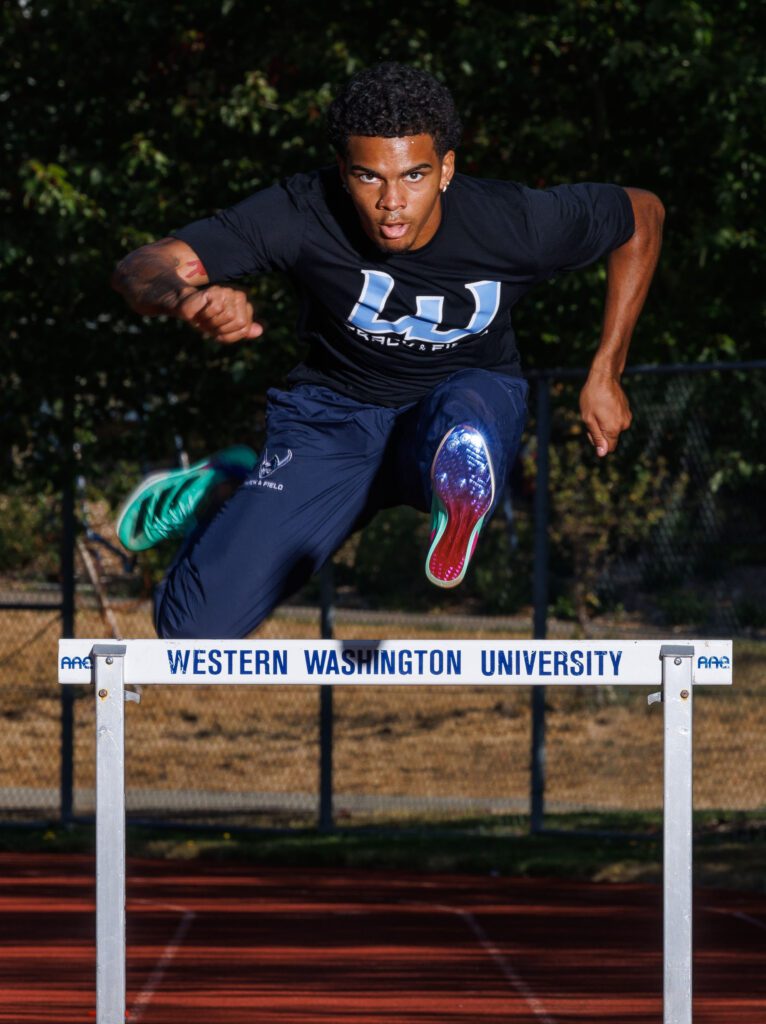 Maurice Woodring runs and leaps over a hurdle with the university's name labeled on the white hurdle.