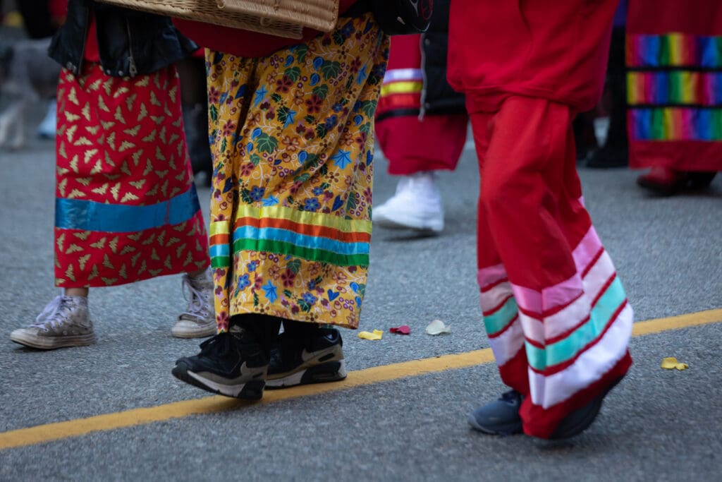 Girls wearing traditional ribbon skirts scatter flower petals at the front of the march.