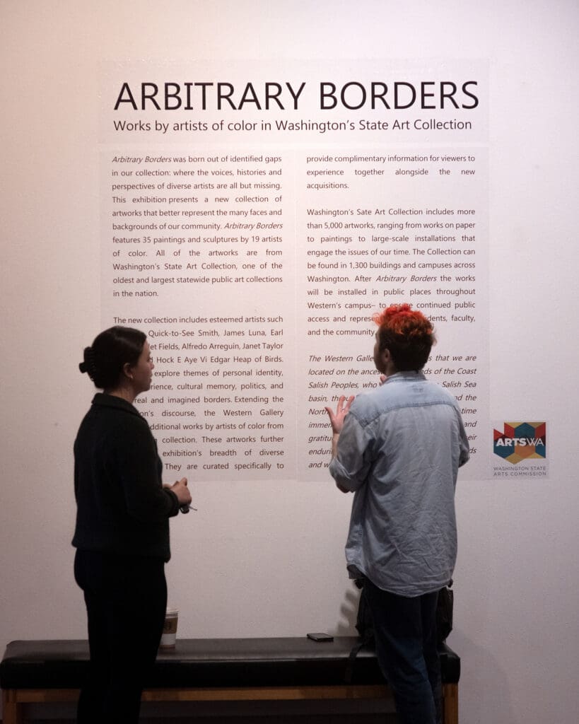 Zoë Fejeran, left, and Quincy Ingalls discuss the exhibit “Arbitrary Borders” in front of the piece with their personal items on the bench in front of them.