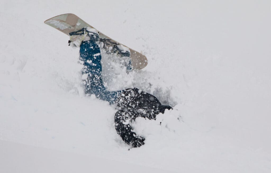 A snowboarder takes a crash face first into the snow.