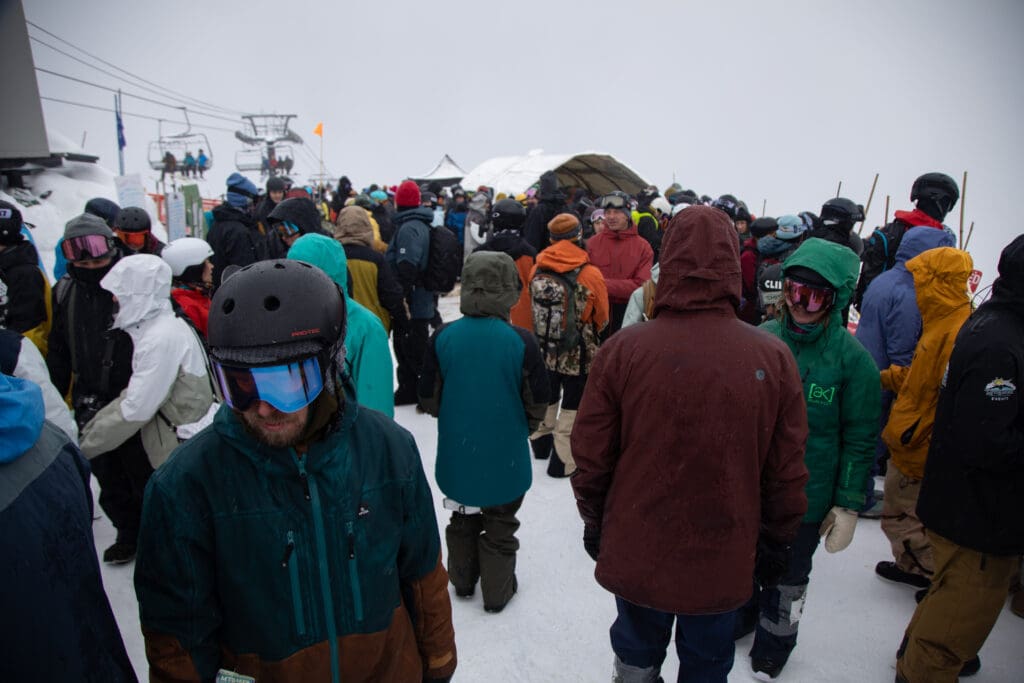 Dozens of racers wait in crowds chatting and eating as they try to keep warm with various different winter jackets, helmets and visors.