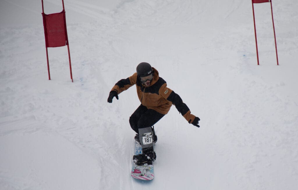 Todd Schlosser finishes his Pro Legends Men race with his arms spread out to maintain his balance on his white snowboard.