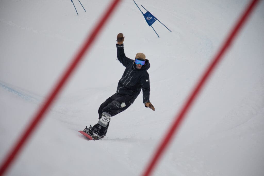 Dusan Kettering of Glacier zooms through the last gates of the Legendary Banked Slalom with one hand raised to balance better on his red snowboard.