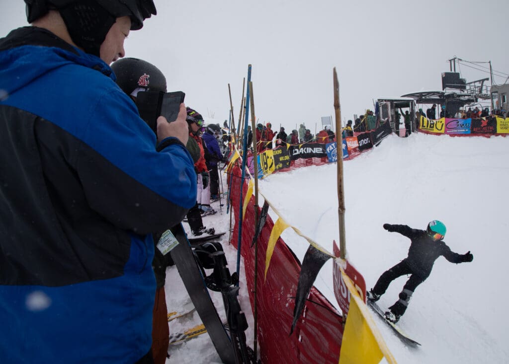 Arland Fagerstrom films his daughter on his phone as his daughter slides by wearing a blue safety helmet.