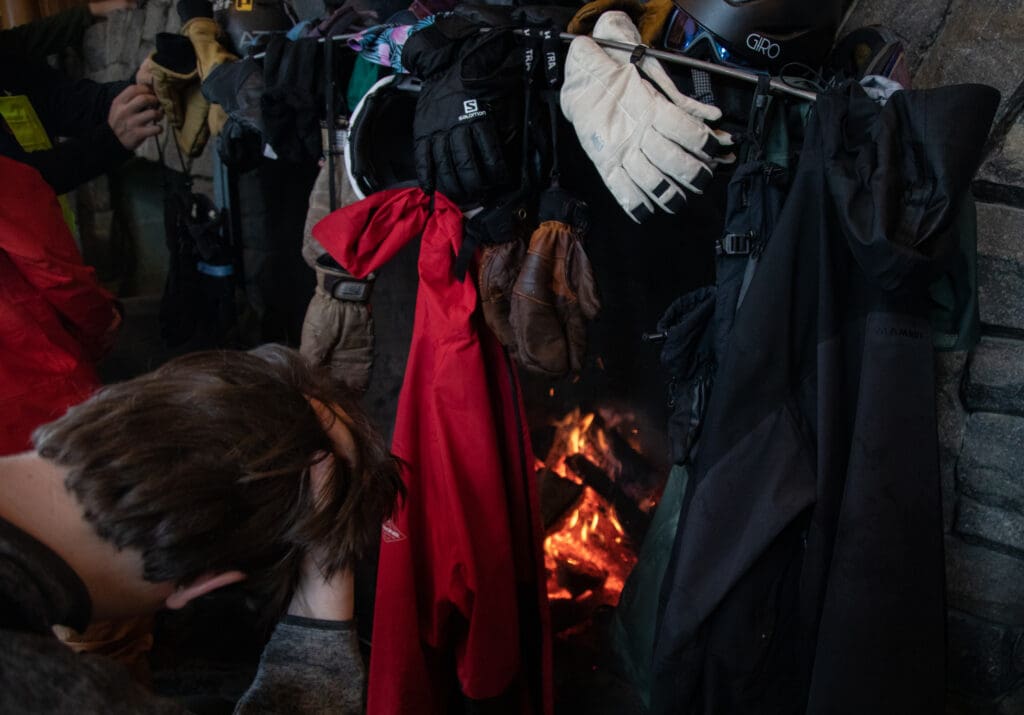 Gloves, coats, scarves, and other clothing articles hang to dry in front of the fire at Raven Hut Lodge.