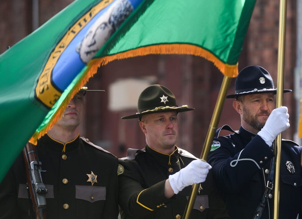 Whatcom County Sheriff's Office and Bellingham Police Department officers carry the Washington state flag, American flag, and Bellingham police flag while wearing official uniforms.