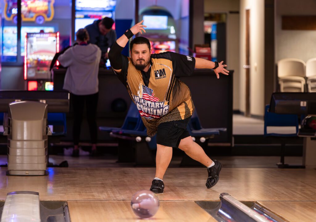 A man in a bowling shirt throws a ball down the lane.