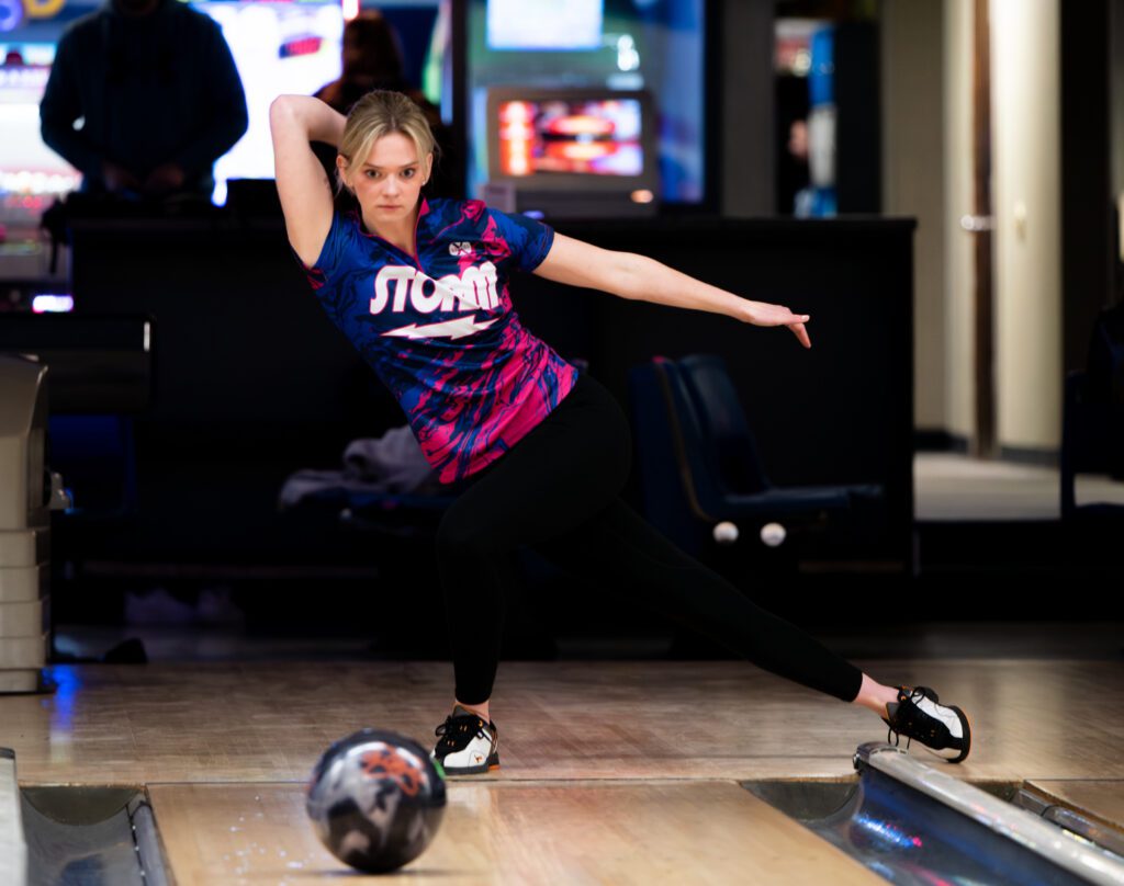 A young woman in a Storm bowling shirt throws a ball on the lane.