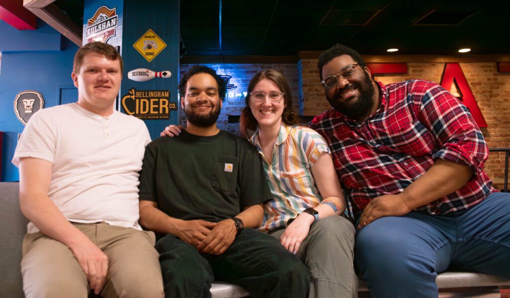 Four people pose for a photo while sitting in a bowling alley.