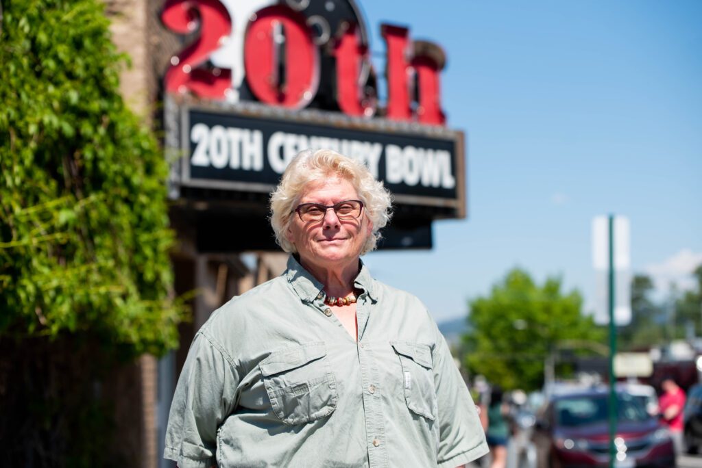 A woman in glasses stands outside a bowling alley. Behind her the sign reads "20th Century Bowl."