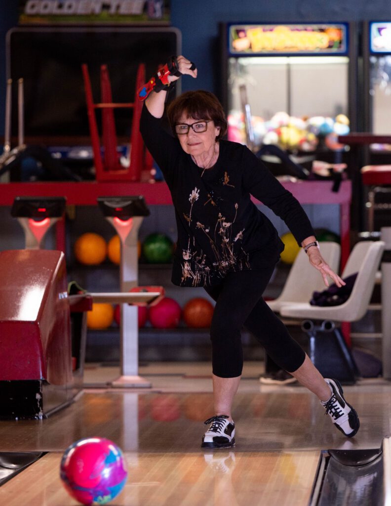 A woman bowls with a pink and purple ball.