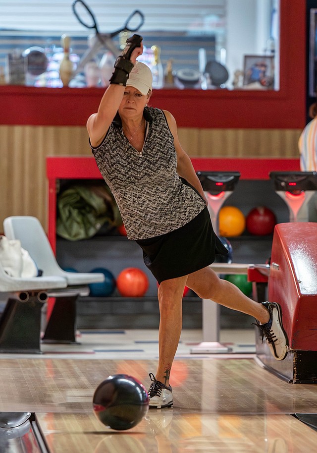 A woman wearing a wrist braces throws a bowling ball on a lane.