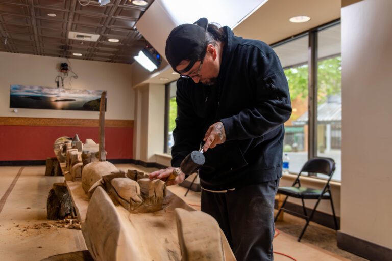 LaClair chisels the story pole from a long piece of wood.