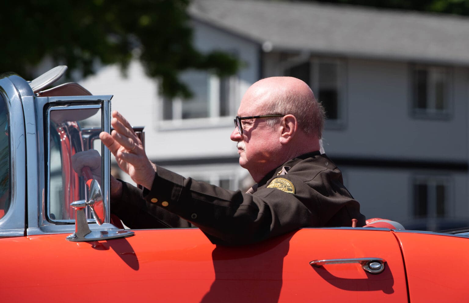 Whatcom County Sheriff Bill Elfo waves while driving an old red Chevrolet.