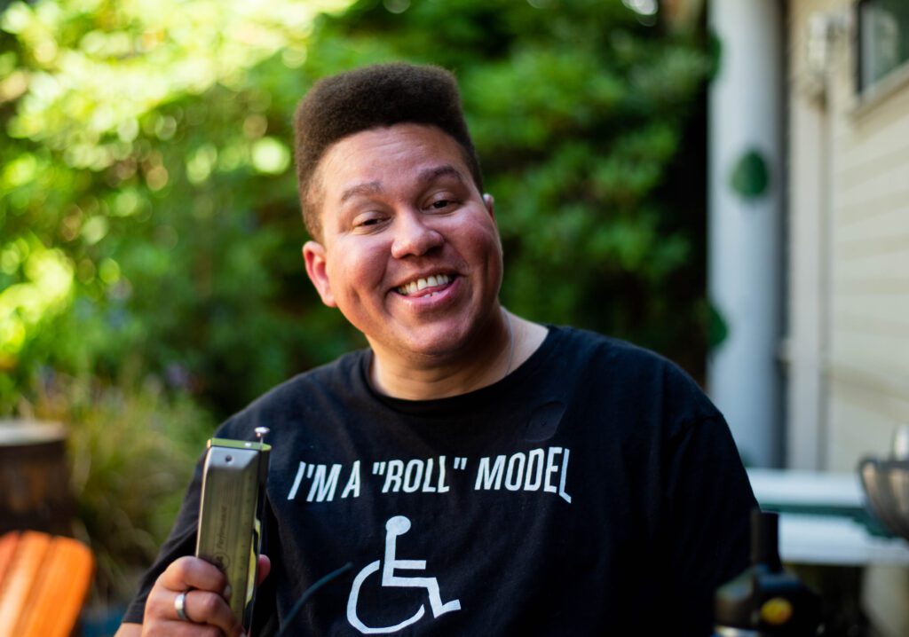 Naaman Hinton smiles while holding his harmonica up.