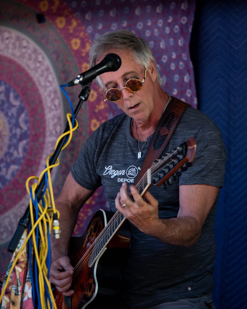 Jon Dalgarn plays the guitar on stage behind a microphone with blue and yellow wires wrapped around.