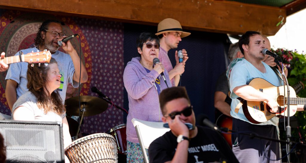 Members of Out of the Ashes sing a song on stage with some performers playing an instrument.