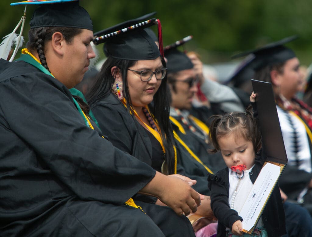 Richard Ahla-tah-mal Johnson, left, and Keisha Kruger watch their daughter play with a diploma during the Northwest Indian College commencement ceremony June 16 at the Lummi Nation Stommish Grounds.