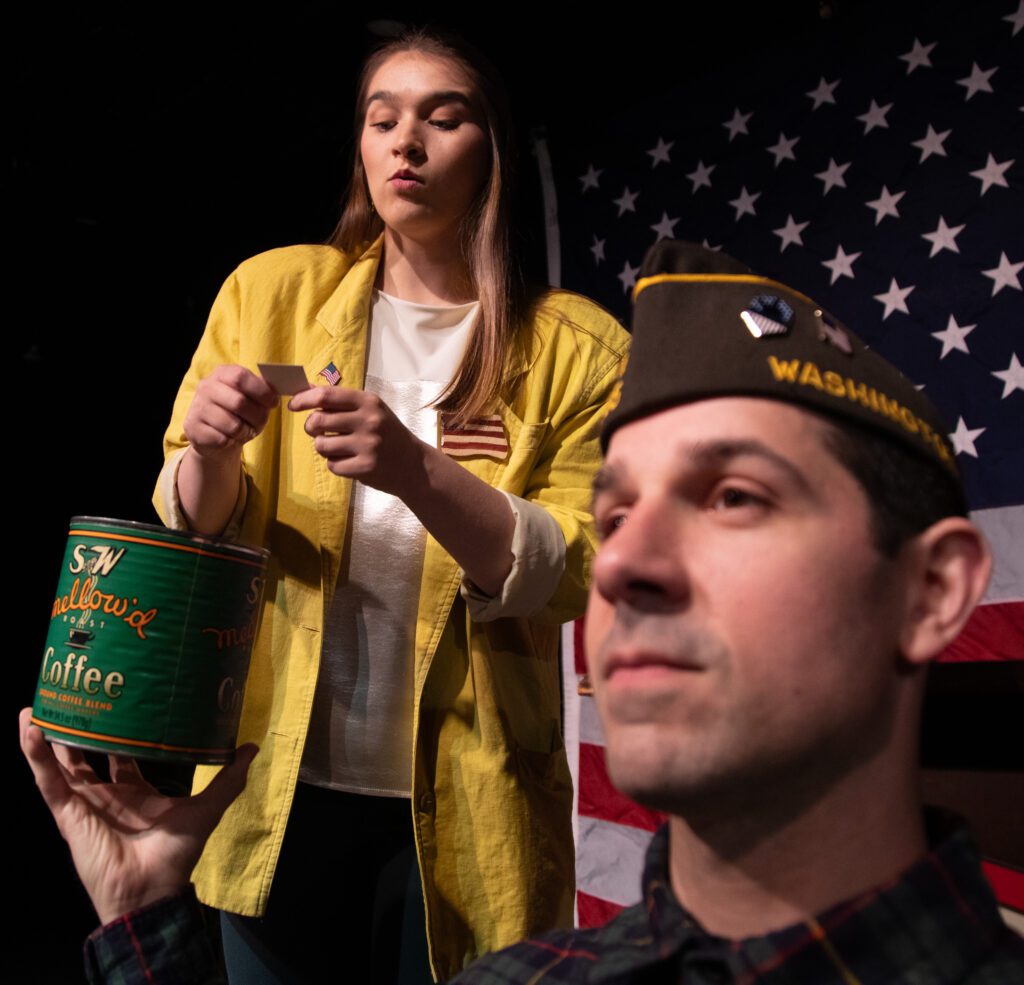 Gabi Gilbride as Heidi Schreck pulls a card from a green vintage coffee can held by Adam St. John on stage.