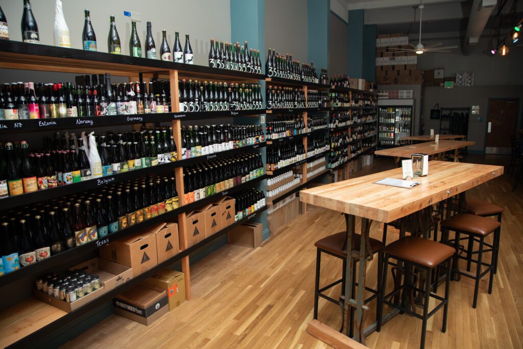 The Great Northern Bottle Shop & Lounge inside where there are tables and chairs next to shelves stacked full of different types of wines, beer, cider, and more.