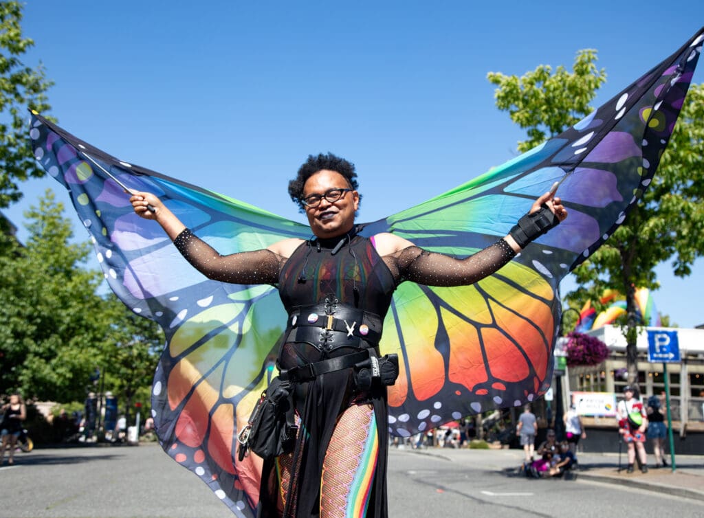 Athena Bell spreads rainbow colored butterfly wings with two poles attached to the ends.