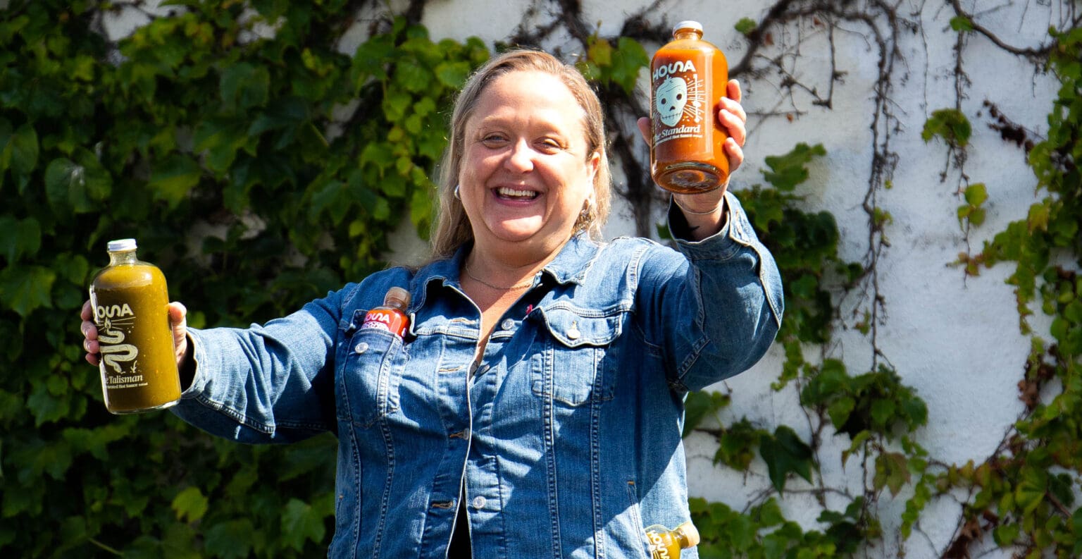 Michelle Schutte, owner of HOSA hot sauce and local artist, shows off some of her favorite sauces with both hands.