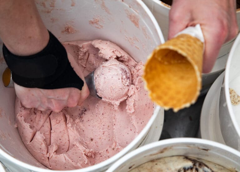 Ellen Fossett scoops strawberry cracked pink pepper ice cream while holding an empty waffle cone.