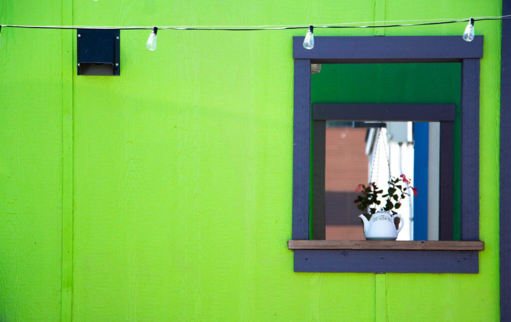 A teapot sits comfortably on the window sill of a neon colored tiny home.