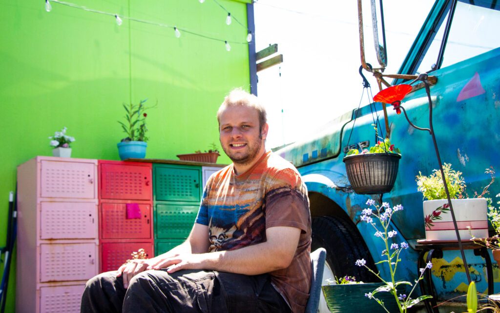 Doug Gustafson, leader of HomesNOW!, sits within the colorful foliage and painted blue truck next to him.