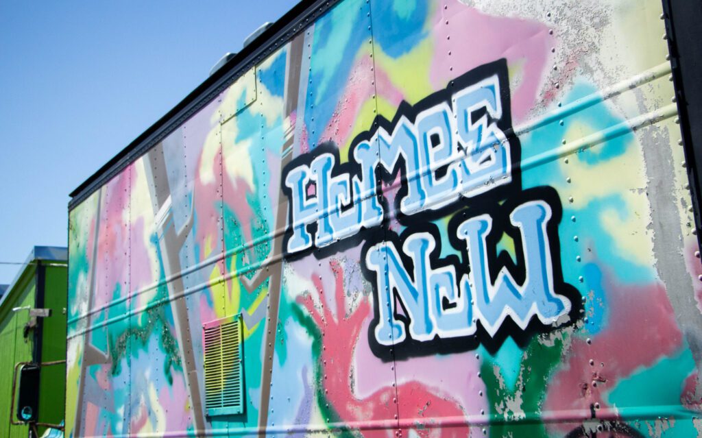 Graffiti on the side of a building has multiple colors and the words "Homes Now" written.