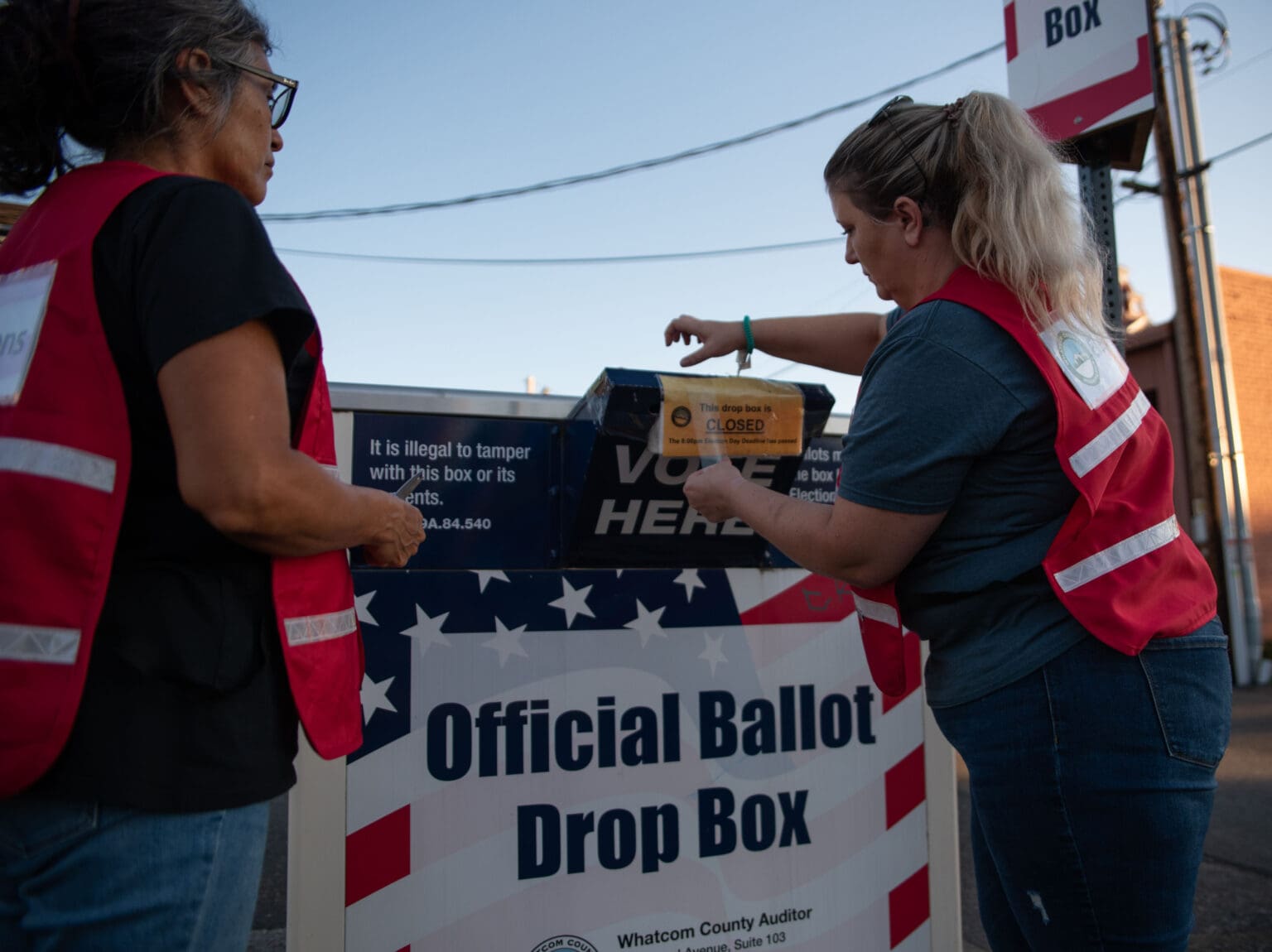 Election officials seal the ballot drop box alongside a helper.