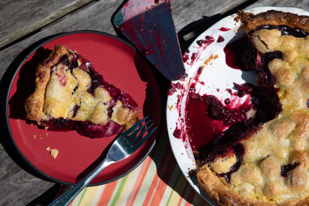 A fresh blackberry pie, courtesy of Erik Burge, sits sliced next to the whole pie with a section missing.