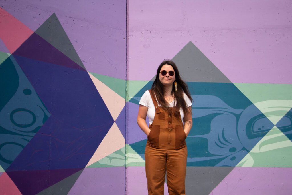 Savannah LeCornu stands in front of the colorful Indigeversal mural.