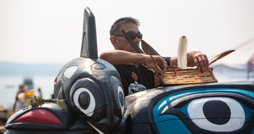 W'tot Lhem, Jay Julius, places a basket with old eagle feathers on the totem.