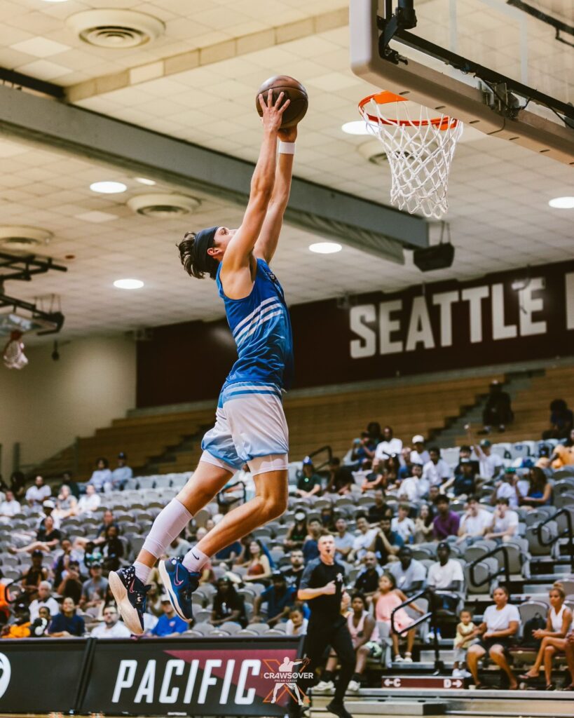 Kai Johnson leaps for a slam dunk with both hands as a referee jogs along with the whistle in his mouth.