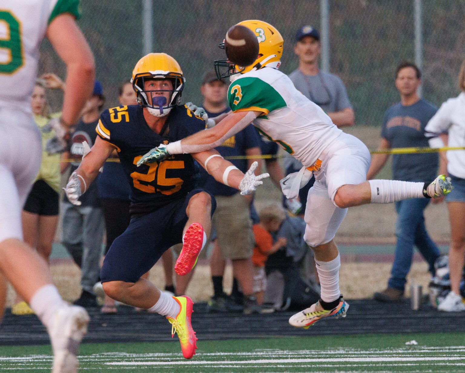 Lynden’s Kaeden Hermanutz breaks up a pass intended for Ferndale's Conner Walcker as they both leap slightly off the grass while a crowd watches from behind a barrier.