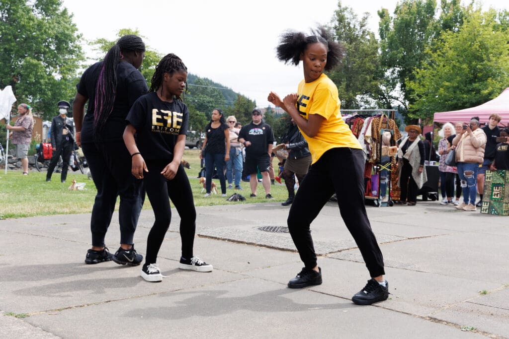 Dancers with the group EFE (Epitome Family Entertainment) perform on the concrete ground in front of a crowd of attendees.