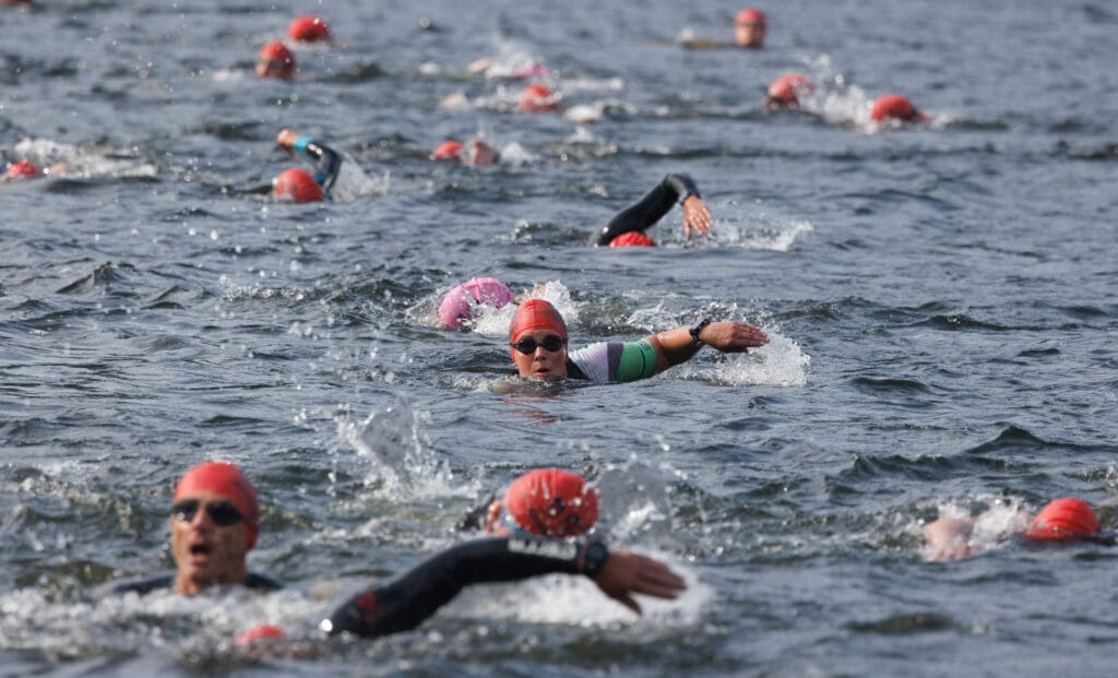 A swimmer looks breaches the water to look how much further they have left as other swimmers splash around them to rush to the finish line.
