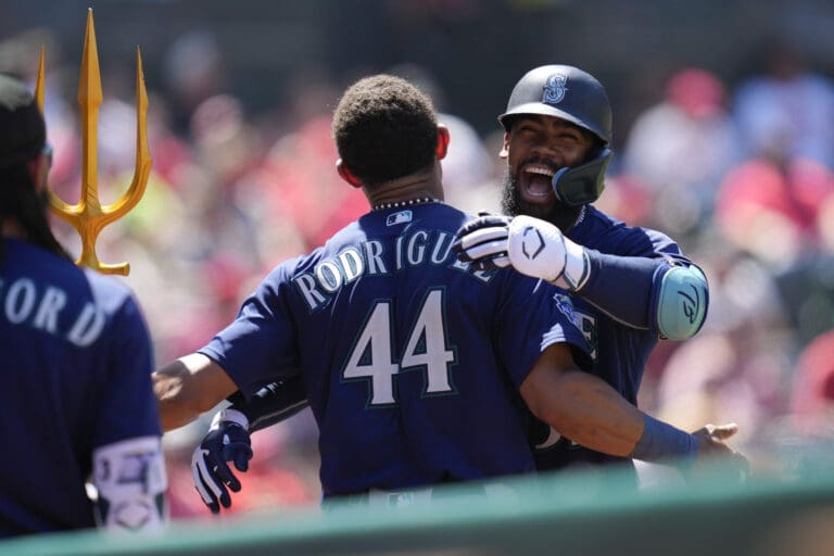 Seattle Mariners designated hitter Teoscar Hernandez, right, celebrates with Julio Rodriguez by hugging next to a teammate holding a trident.