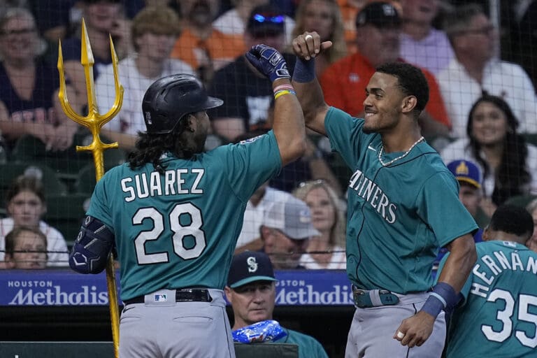 Seattle Mariners' Eugenio Suarez celebrates with Julio Rodriguez by giving each other an elbow bump in front of the crowd watching from the bleachers.