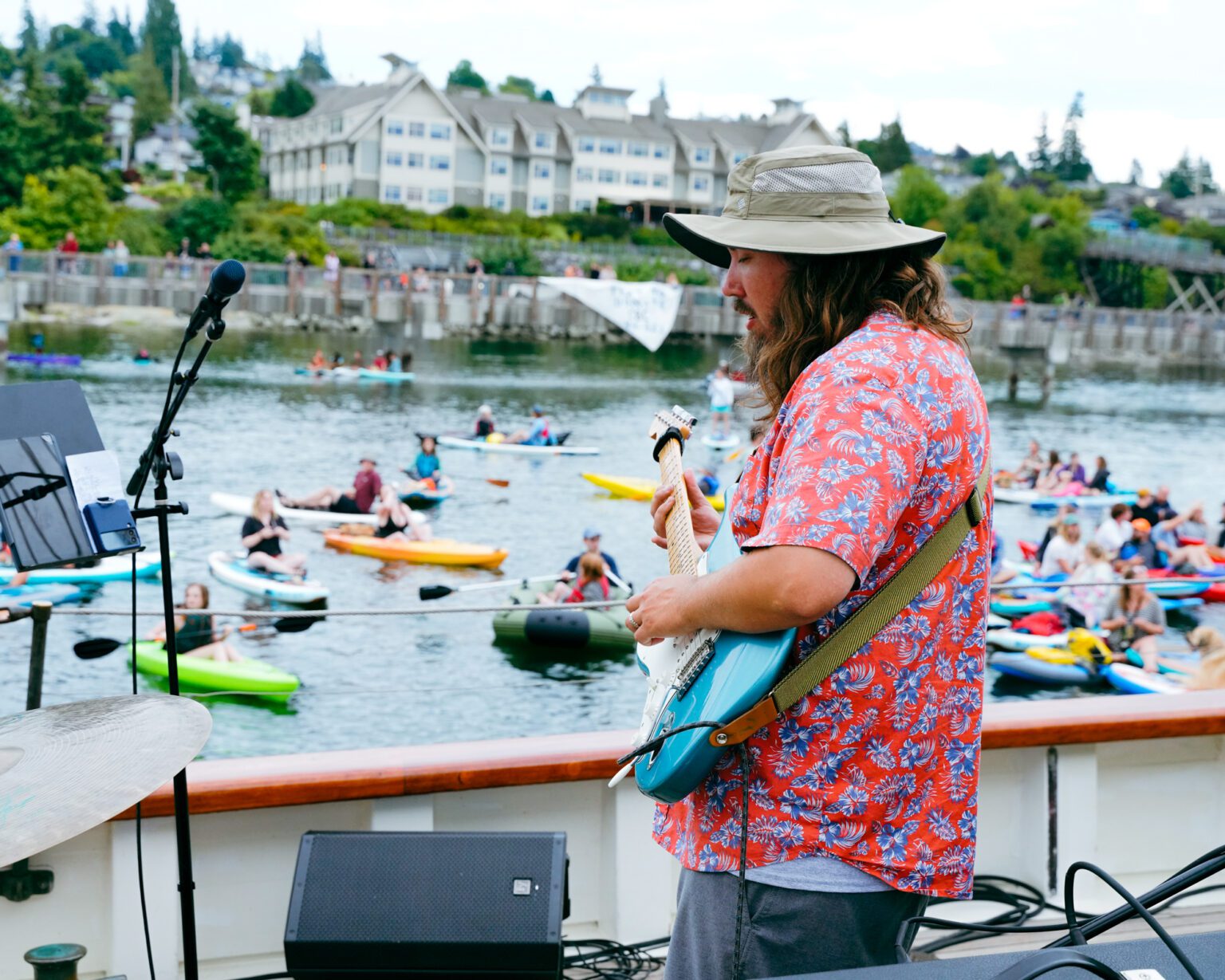 A man plays an electric guitar as many kayakers idle nearby to listen.