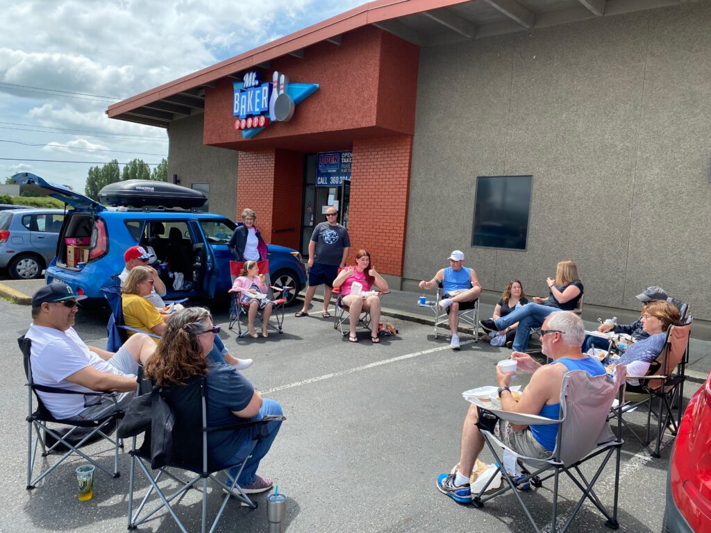 A group of people sit in camping chairs outside a bowling alley.