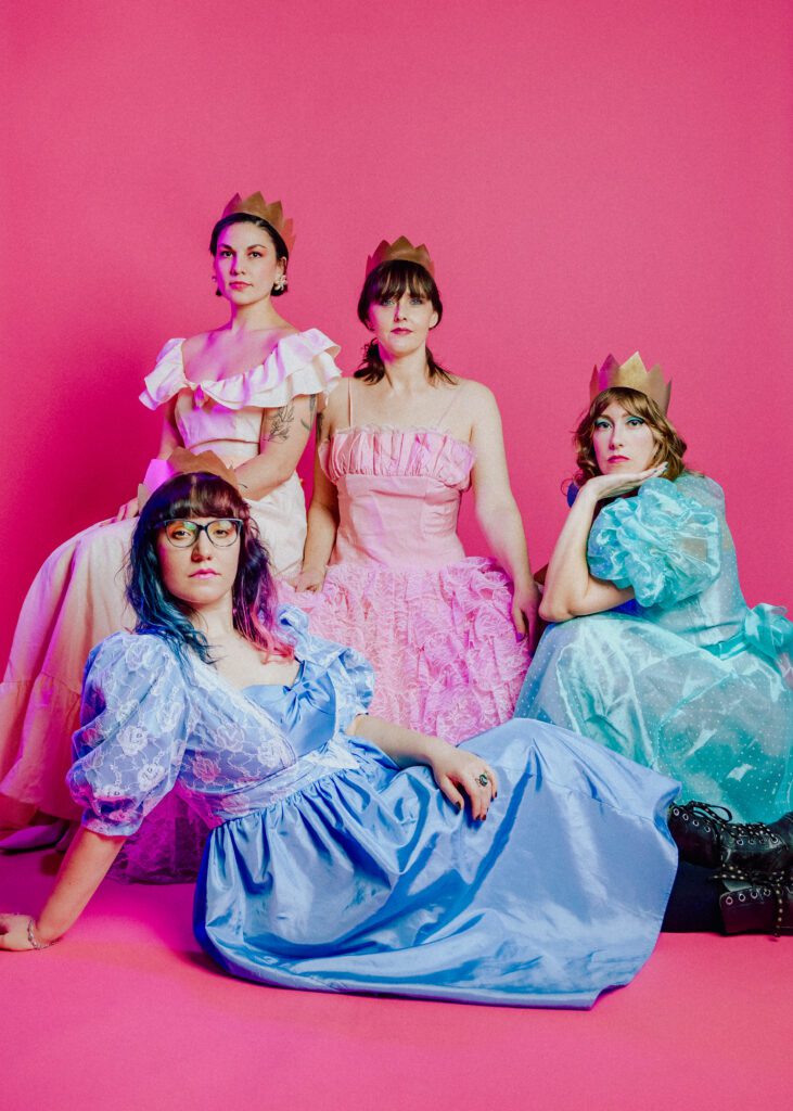 Cat Valley group poses for a photo on a bright pink background while members wear gold crowns and colorful dresses.