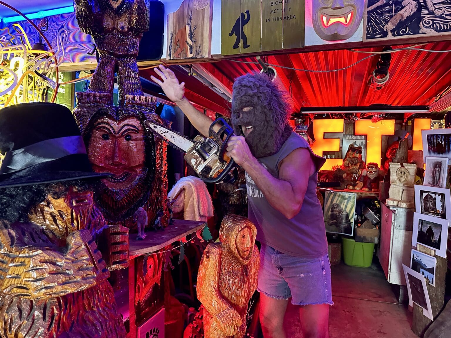 Michael Vail, wearing a Bigfoot costume, shows off some of the wood carvings and statues as he gestures towards his handmade carvings.