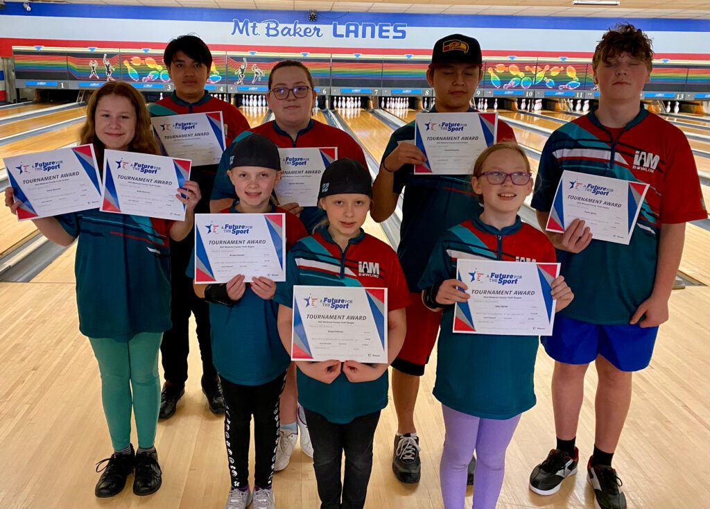 A group of junior bowlers hold awards in a bowling alley.