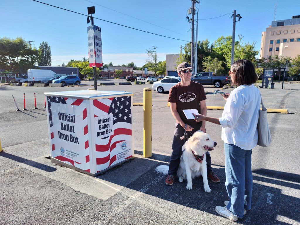 News intern Simone Higashi, right, interviews Tyler Ritchie and his dog, Marvin, next to the ballot box.