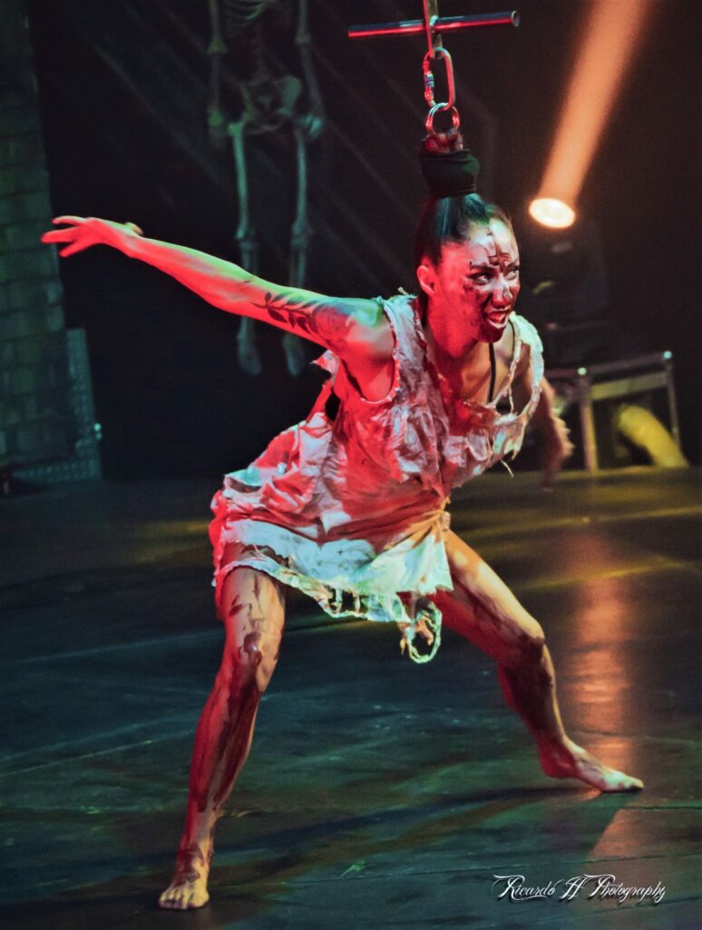 Performer Livia Marciano dressed in a bloody costume looks to the audience with white eye contact lenses.